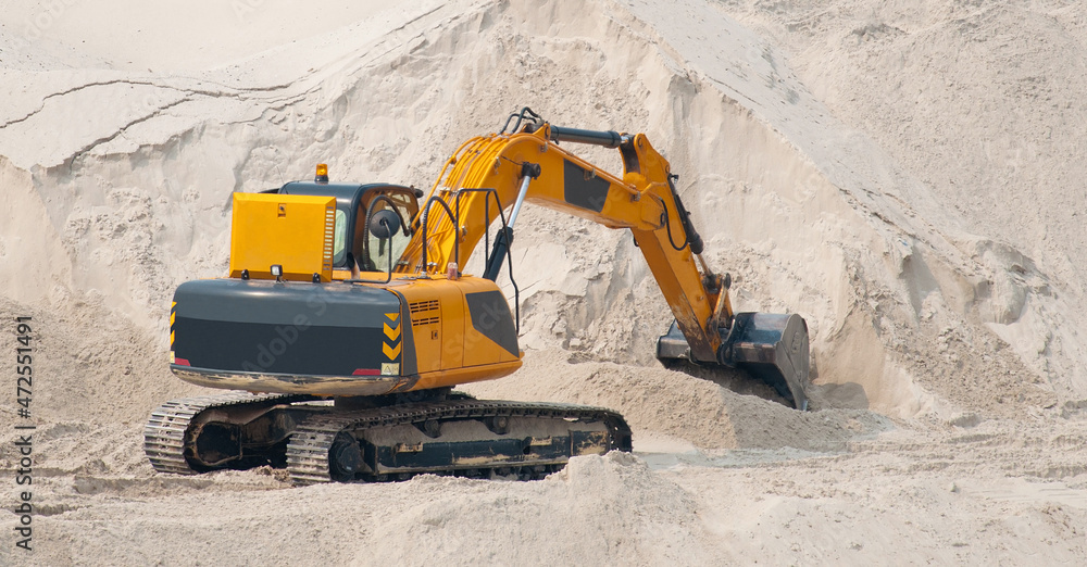 The excavator works against a background of a pile of sand. The excavator works against a background of a pile of sand.