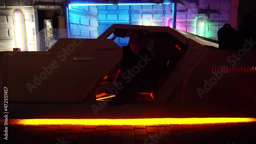Cyberpunk concept. Strange character with punk-type haircut gets out of futuristic car in street at night. Neon lighting. Science fiction scene, fantasy. World of tomorrow. photo