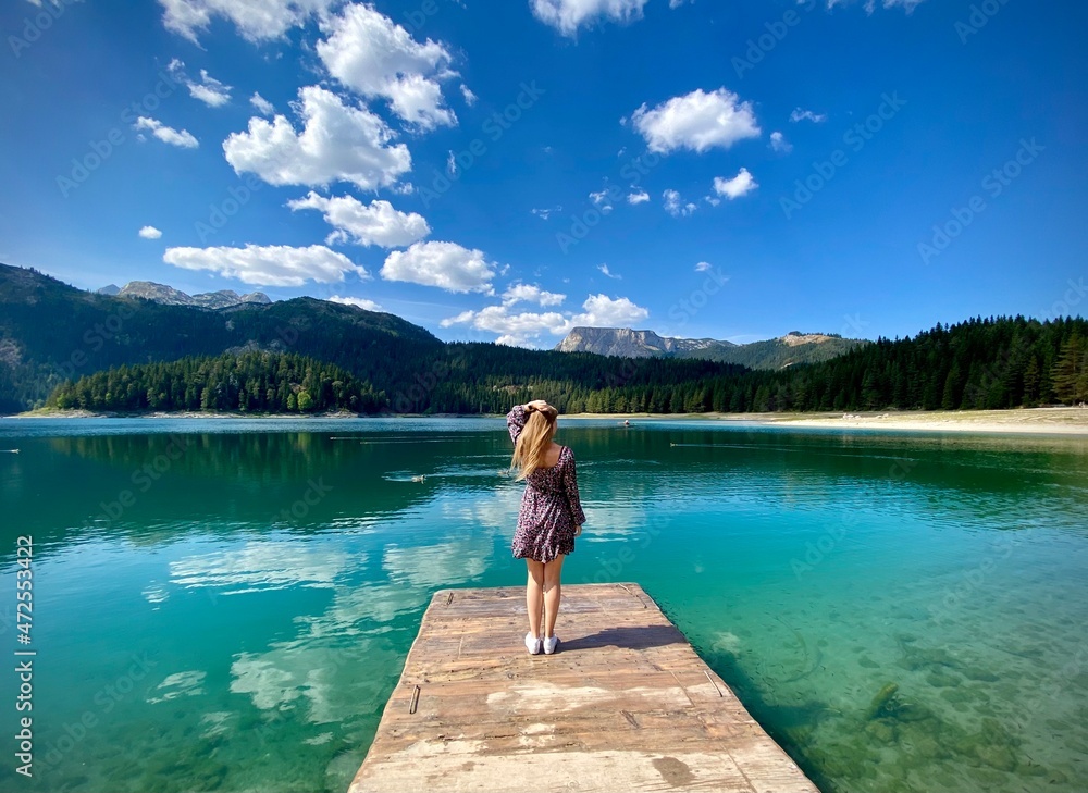 An amazing lake and blue sky, a little bridge and a blond girl standing on it. Concept of solitude, relaxing, amazing nature and human. An amazing lake and blue sky, a little bridge and a blond girl standing on it. Concept of solitude, relaxing, amazing nature and human.