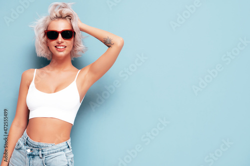 Young beautiful smiling female in trendy summer clothes. Sexy carefree woman posing near blue wall in studio. Positive blond model having fun and going crazy