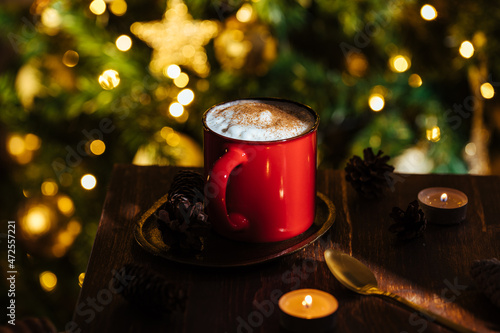 Cup of pumpkin spice late in a rustic moody and vintage Christmas atmosphere and Christmas lights and tree in blurry background
