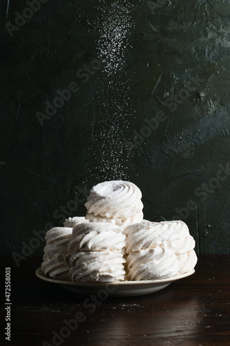 Lots of marshmallows on a plate sprinkled with powdered sugar, on a dark background with a place to insert text