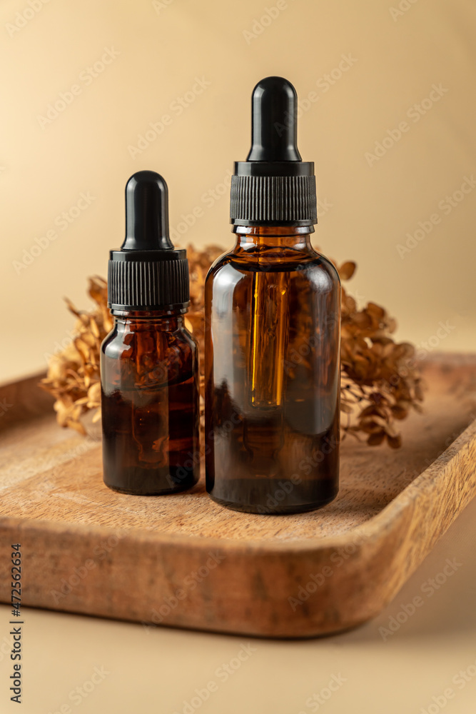Cosmetic glass bottles with dropper on wooden tray with dry hydrangea flower. The concept of beauty salon and natural cosmetics. Cosmetic glass bottles with dropper on wooden tray with dry hydrangea flower. The concept of beauty salon and natural cosmetics.