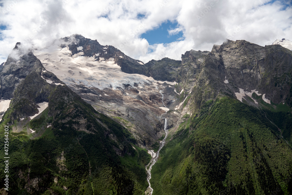 Caucasus mountains. Glacier turning into the river. Mountains in the clouds. Beautiful snow-capped mountains in summer.