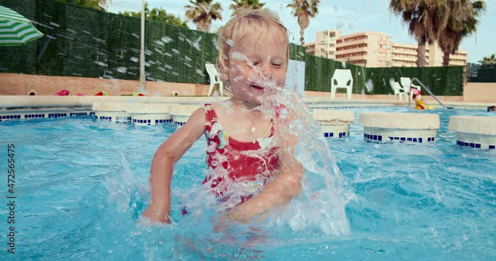 Young baby girl playing with water in the swimming pool on vacation in