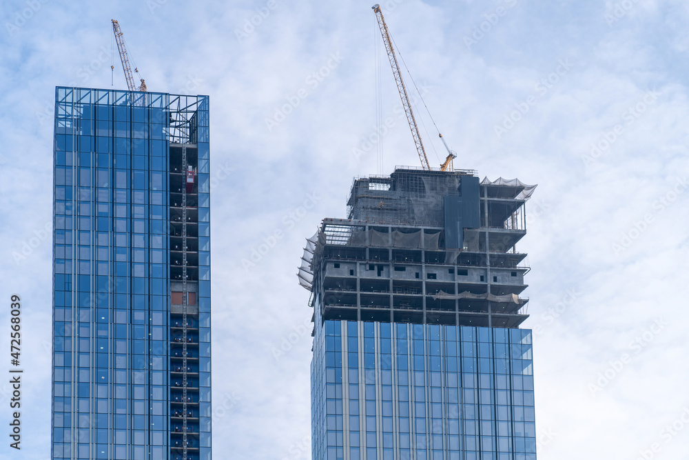Construction cranes and unfinished residential buildings against blue sky with clouds. Housing construction, apartment block with scaffolding Construction cranes and unfinished residential buildings against blue sky with clouds. Housing construction, apartment block with scaffolding