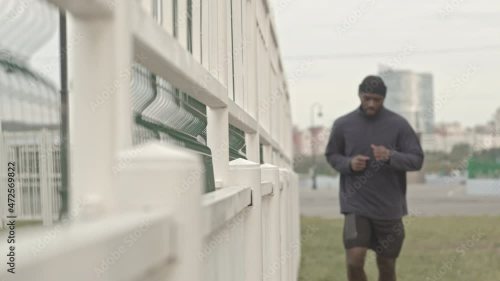 Slowmo shot of fit African-American male athlete in activewear taking short break to have a rest while jogging outdoors on cold morning Slowmo shot of fit African-American male athlete in activewear taking short break to have a rest while jogging outdoors on cold morning