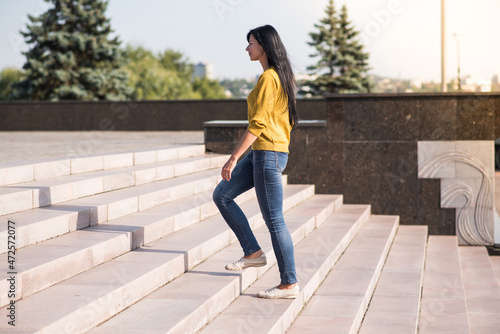 A young, beautiful and attractive Caucasian brunette girl in a yellow sweater climbing up the stairs.