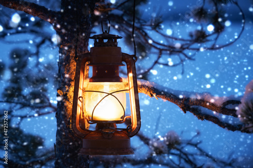 Christmas lantern in magic winter evening snowy forest hanging on snow covered tree. Beautiful winter natural background with kerosene lamp. New year and Christmas Holiday concept.