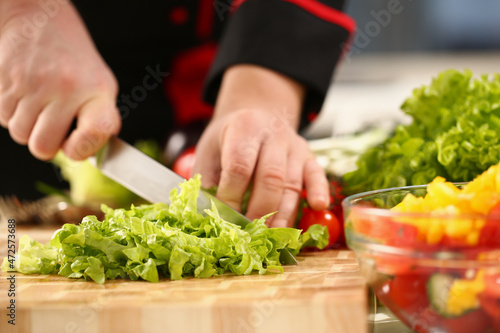 A male chef cuts a green salad with a knife