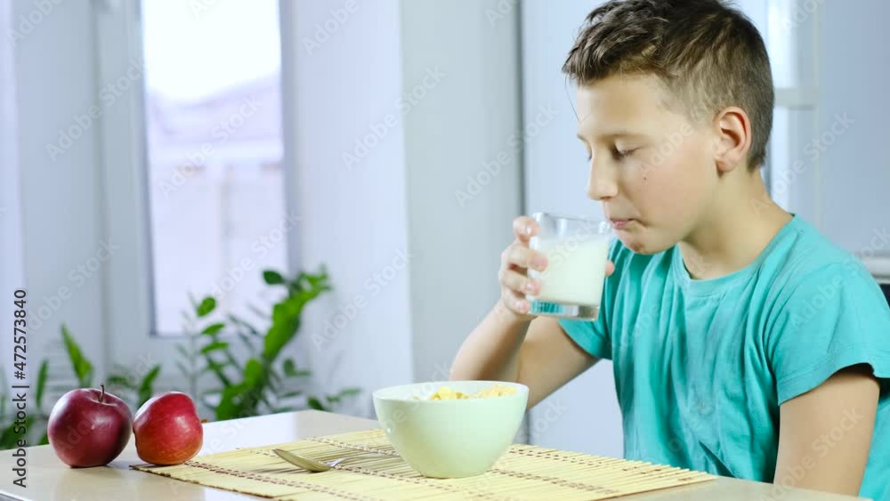 Boy eat cornflakes and drink milk for breakfast. Slowmotion. Healthy breakfast. Home kitchen background Boy eat cornflakes and drink milk for breakfast. Slowmotion. Healthy breakfast. Home kitchen background