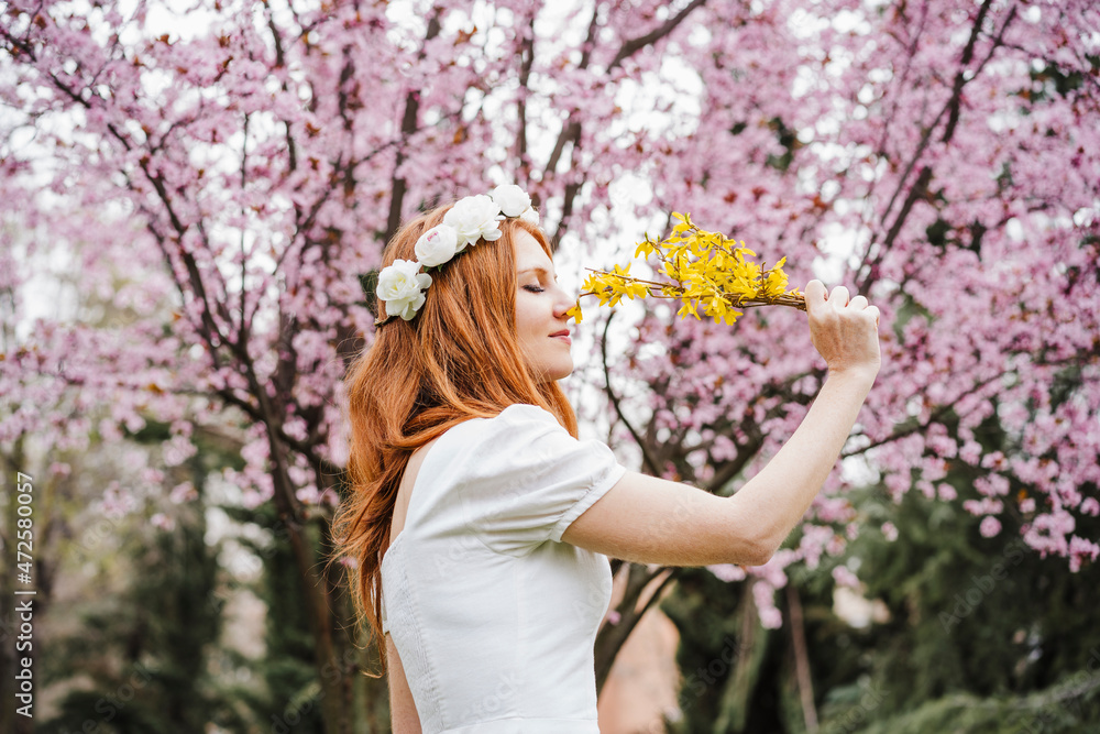 Beautiful woman smelling yellow flower while standing in front of almond tree at park Beautiful woman smelling yellow flower while standing in front of almond tree at park
