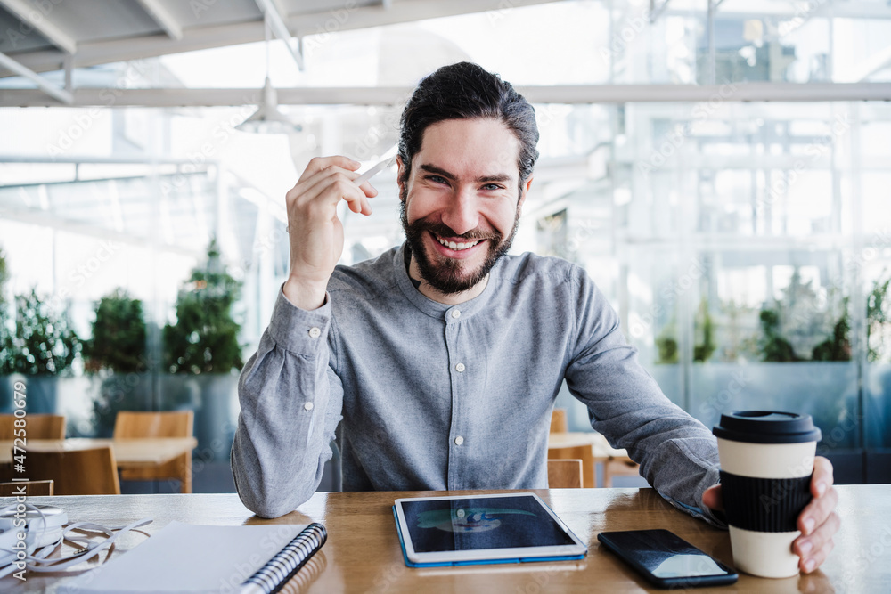 Smiling male freelancer with reusable coffee cup by wireless technologies in office Smiling male freelancer with reusable coffee cup by wireless technologies in office