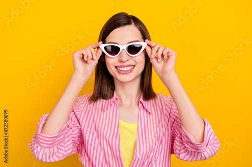 Photo of adorable glad positive lady arms touch sunglass beaming smile isolated on yellow color background