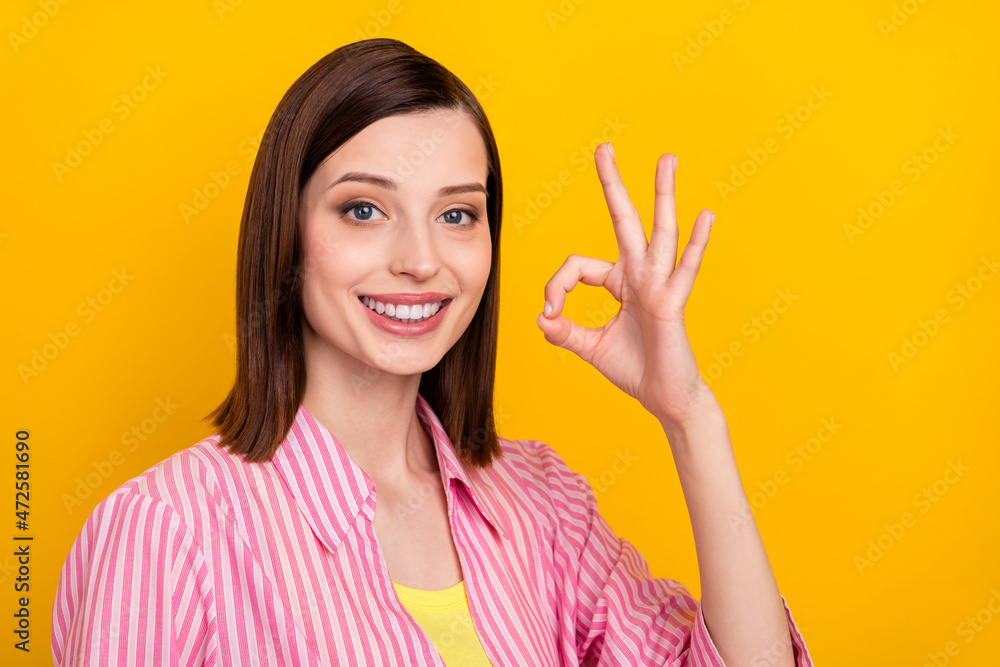 Photo of pretty positive person fingers show okey symbol beaming smile isolated on yellow color background Photo of pretty positive person fingers show okey symbol beaming smile isolated on yellow color background