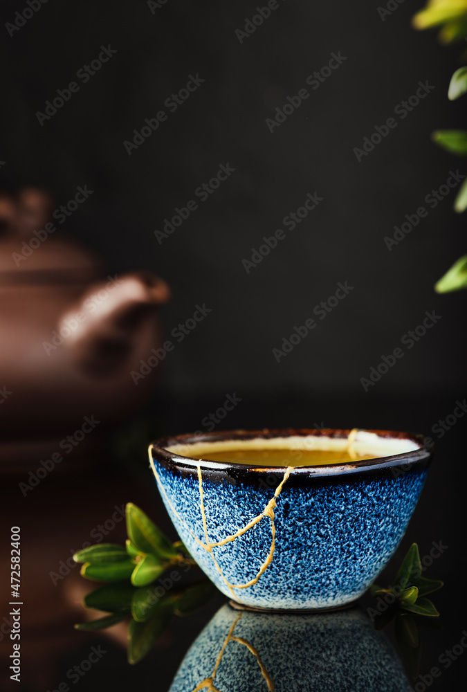 Cup of green Japanese tea on a dark background. Selective focus on the cup. Reclaimed ceramic blue cup, second life of things, recycling or kintsugi Cup of green Japanese tea on a dark background. Selective focus on the cup. Reclaimed ceramic blue cup, second life of things, recycling or kintsugi