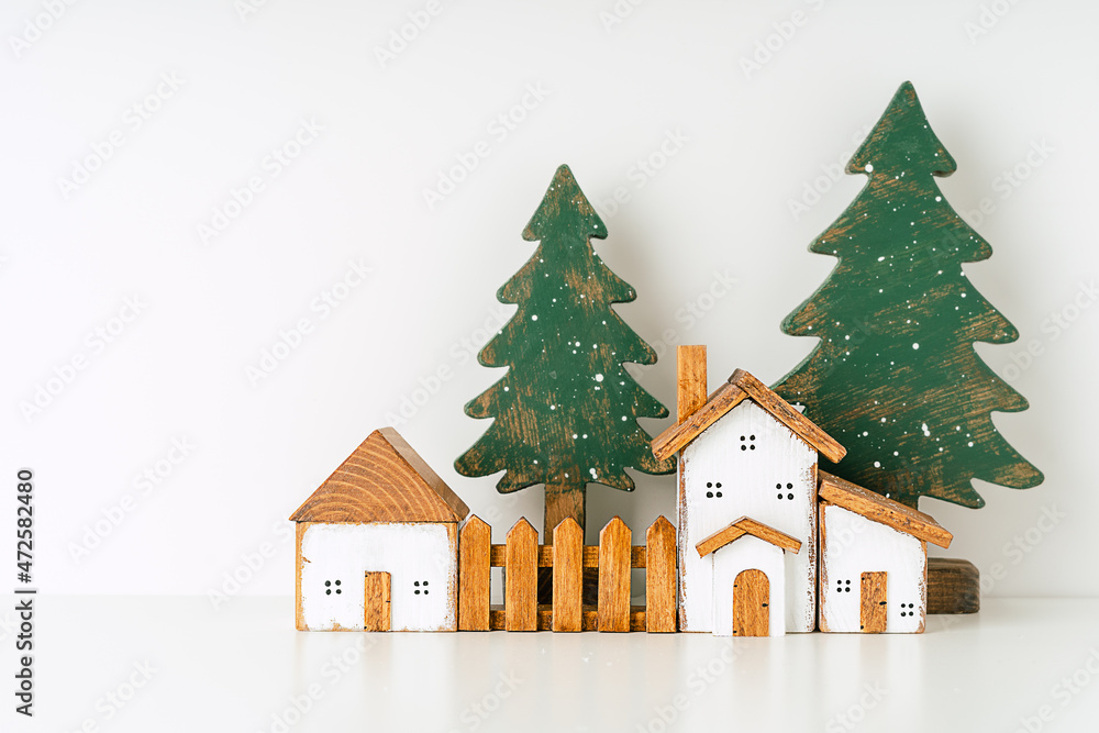 Naklejka premium Happy New Year and Merry Christmas postcard. Festive white background with toy wooden house, snow, rustic christmas tree, village and decoration. Copy space for winter holidays greeting card.