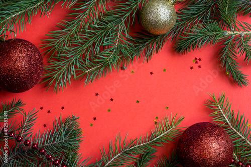 Red background with Christmas decorations from fir branches and Christmas balls. Bright red Christmas and New Year background, Free space for your text. Natural spruce branches.