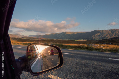 View from a car on a mountains and reflection in car mirror of sun rise over mountain peak and concrete mixer truck passing by. Connemara, county Galway, Ireland. Car travel with stunning scenery.