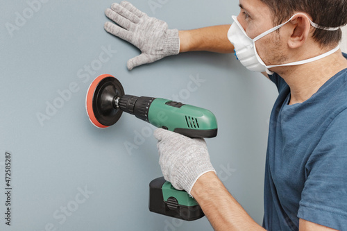 Photography Young handyman wearing respirator grinding wall with disc sanding machine