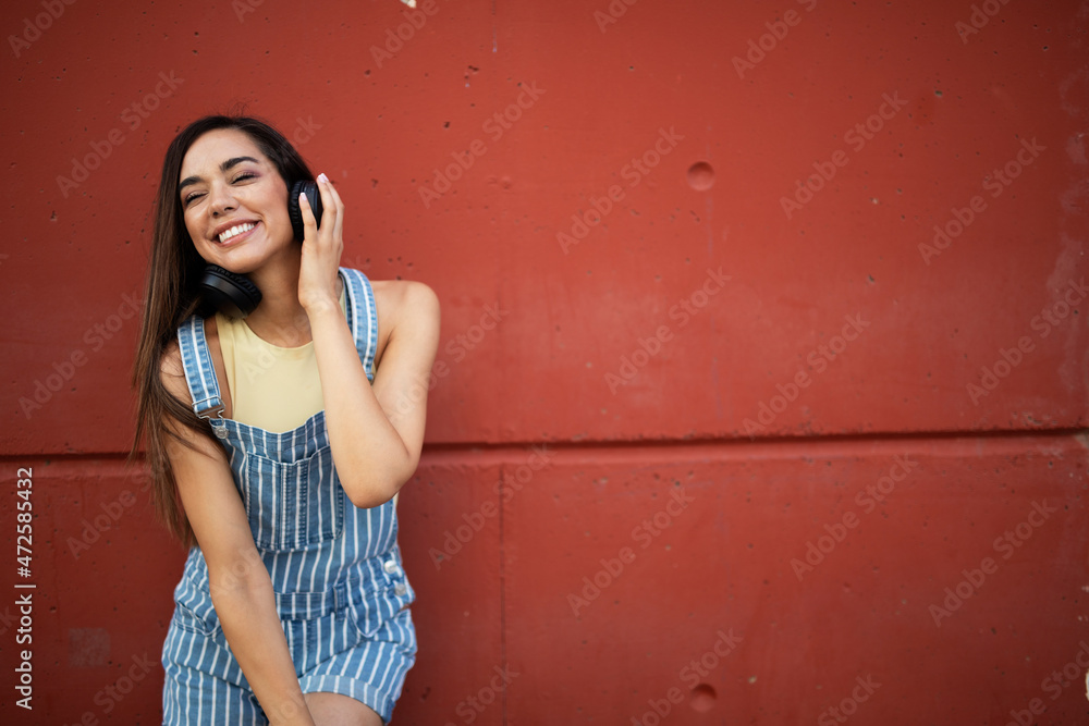 Fototapeta premium Young happy woman listening to music outdoors. Positive hipster girl with headphones enjoying in sunny day..