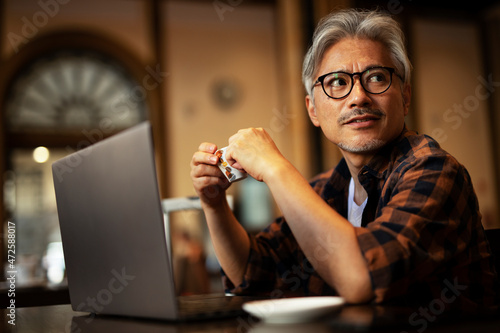 Businessman working on laptop in cafe. Handsome senior man enjoying in fresh coffee..