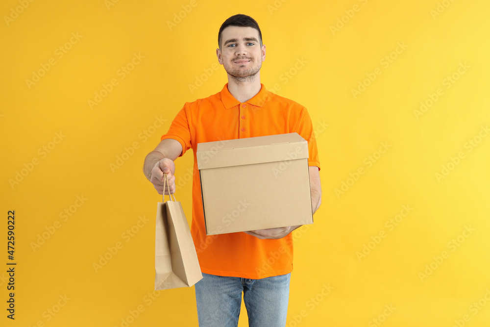 Delivery man holds box and paper bag on yellow background Delivery man holds box and paper bag on yellow background