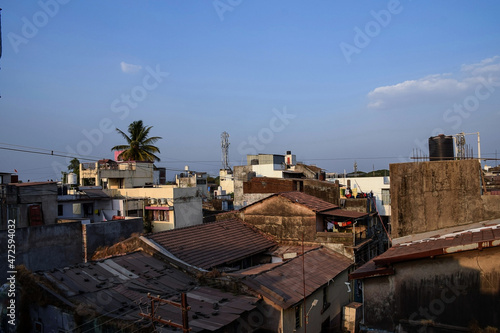 Stock photo of beautiful sunset view from the terrace in the old residential area. Group of building and houses with clay made roof tiles., plam tree, self supporting tower, at Kolhapur, India.