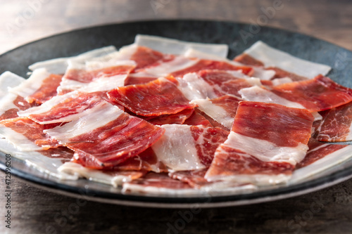 Spanish serrano ham slices on black plate on wooden table
