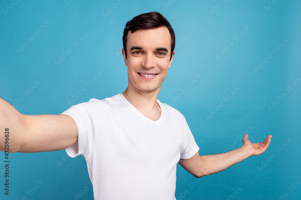 Photo of young handsome man make selfie gesture hand empty space welcome isolated over blue color background Photo of young handsome man make selfie gesture hand empty space welcome isolated over blue color background