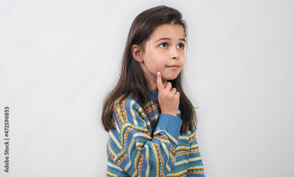 Pensive child wearing colorful sweater looking at one side posing over light grey studio background. A thoughtful little girl thinking about something. Pensive child wearing colorful sweater looking at one side posing over light grey studio background. A thoughtful little girl thinking about something.