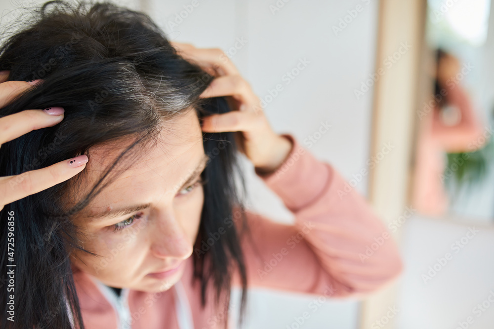 Portrait of a beautiful young woman examining her scalp and hair in front of the mirror, Portrait of a beautiful young woman examining her scalp and hair in front of the mirror,