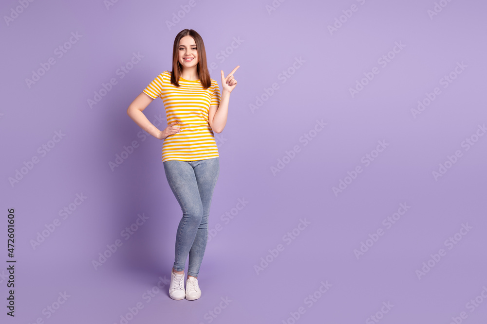 Full body photo of young cheerful girl indicate finger empty space promo suggest direct ads isolated over purple color background Full body photo of young cheerful girl indicate finger empty space promo suggest direct ads isolated over purple color background
