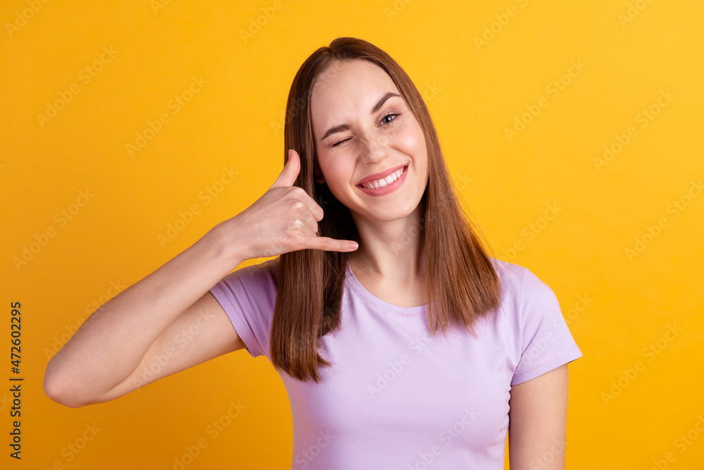 Photo of young cheerful girl show fingers call symbol wink eye isolated over yellow color background Photo of young cheerful girl show fingers call symbol wink eye isolated over yellow color background