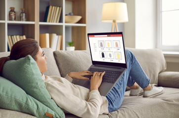 Young woman lying relaxing on sofa at home shopping online on internet on computer. Millennial girl rest couch buy purchase on laptop black Friday or seasonal sales. Promotion and discount.
