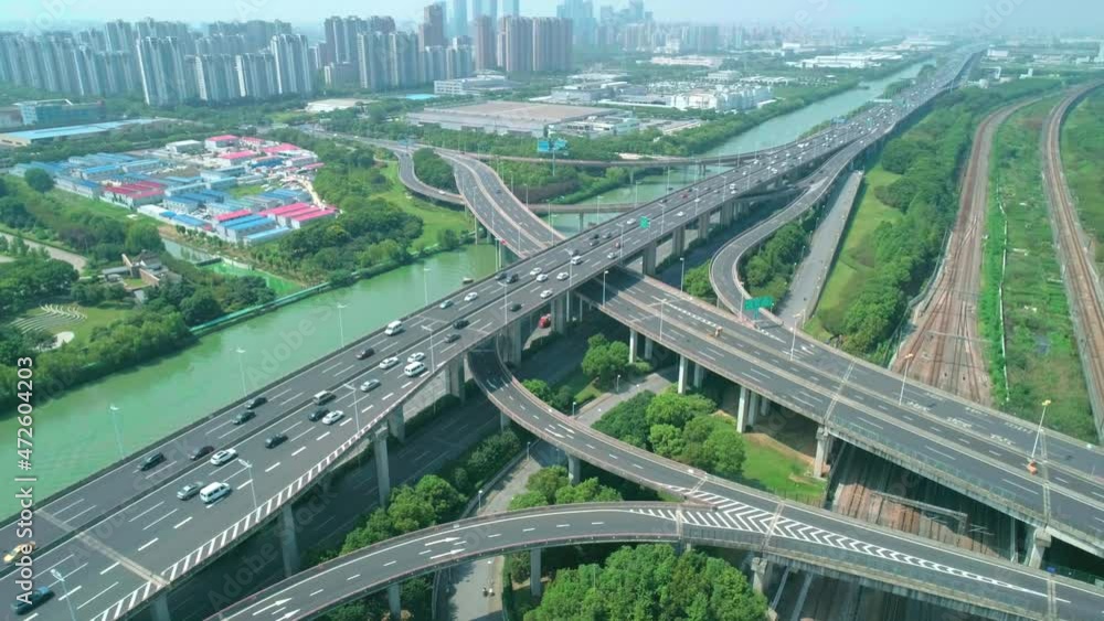 Aerial orbital view of a highway overpass multilevel junction with fast moving cars surrounded by green trees and with a river on a side on a sunny day Aerial orbital view of a highway overpass multilevel junction with fast moving cars surrounded by green trees and with a river on a side on a sunny day