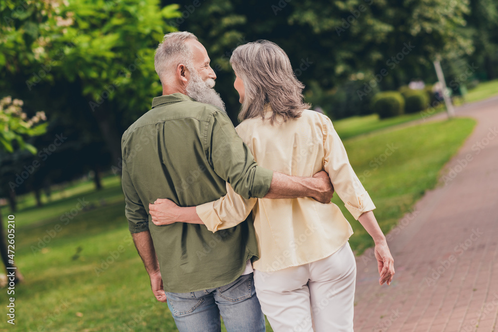 Back photo of nice expression old grey hair couple go hug wear casual shirts outdoors walk in park