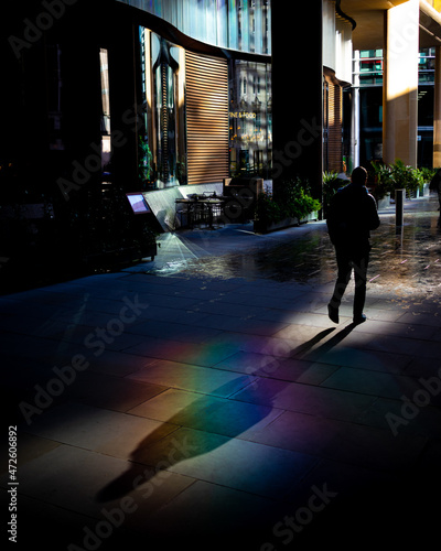 a man walks through the city casting his shadow across the colourful refracted light on the floor