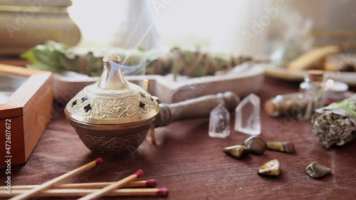 Detail of a burner of medicinal herbs with smoke coming out on an altar to perform energy cleansing and witch rituals with various bundles, stones and crystals photo