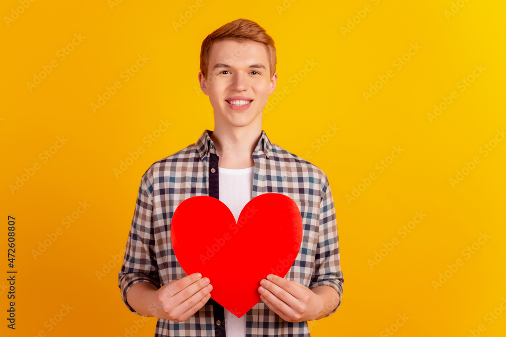 Photo of young man hold paper heart valentine day romantic feelings isolated over yellow color background Photo of young man hold paper heart valentine day romantic feelings isolated over yellow color background