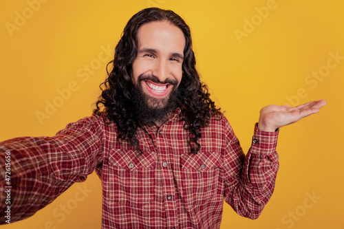 Positive brunet guy shoot selfie hand presenting empty space sale option novelty isolated on yellow background