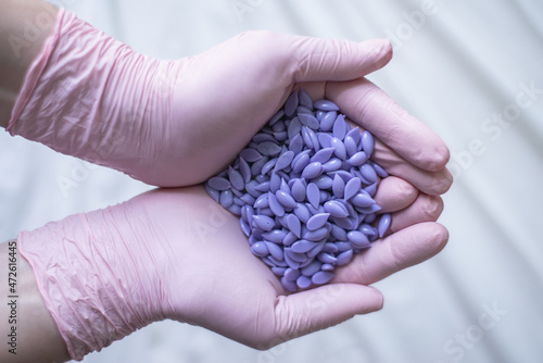 Depilation master holds purple hair removal wax in pink gloves
