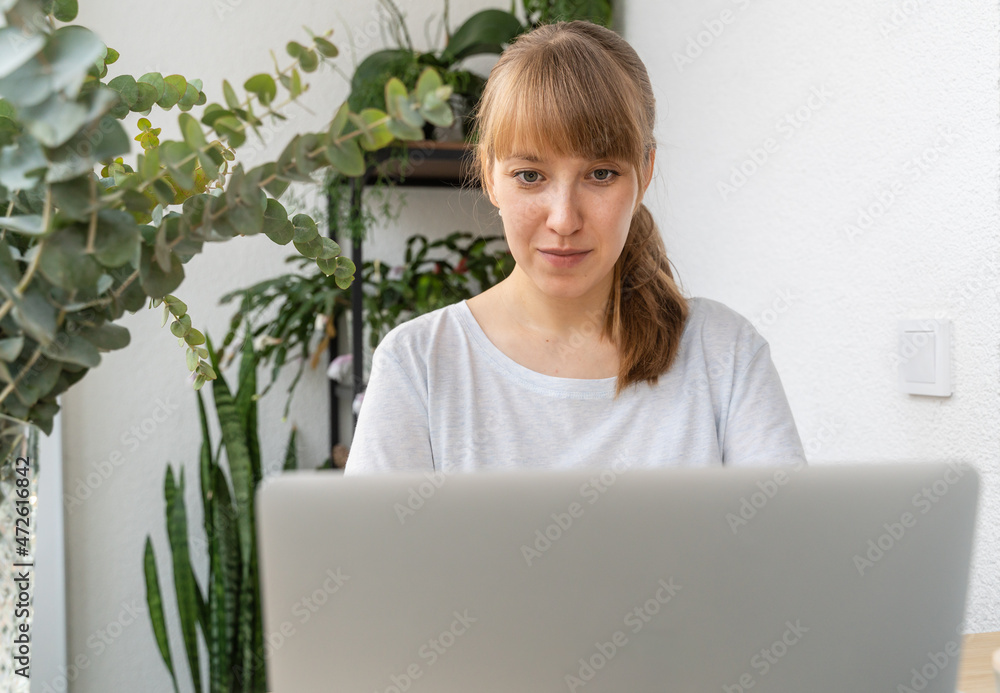 Woman working on laptop surrounded by plants and flowers on balcony at daytime Woman working on laptop surrounded by plants and flowers on balcony at daytime