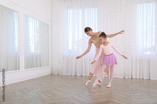 Little ballerina and her teacher practicing dance moves in studio. Space for text