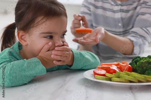 Mother feeding her daughter indoors, closeup. Little girl refusing to eat vegetables photo