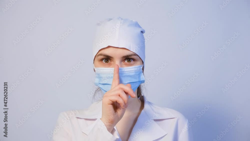 A doctor looks around, shows a sign of silence finger at the mouth, a gesture of silence. A doctor looks around, shows a sign of silence finger at the mouth, a gesture of silence.
