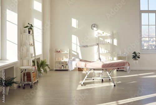 Beautiful interior of new empty massage room, spa center, beauty salon, or dermatological clinic with massage bed, magnifying lamp, and shelves and wall racks with modern cosmetic skin care products photo