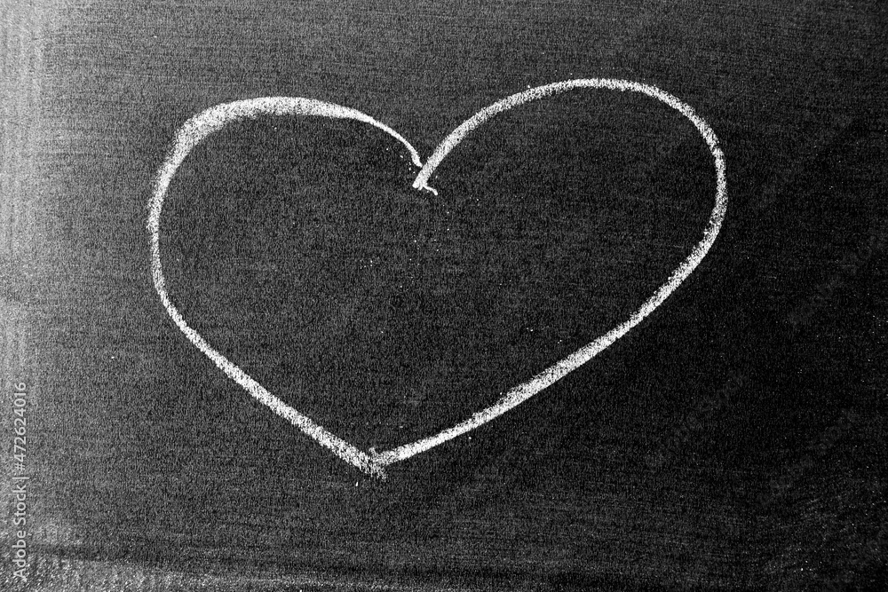 White color chalk hand drawing in heart shape on blackboard or chalkboard background White color chalk hand drawing in heart shape on blackboard or chalkboard background