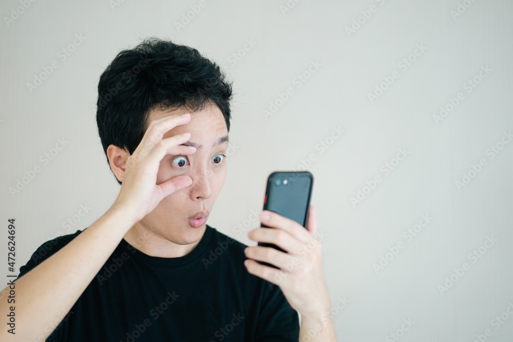 Funny - excited Asian young man touching his eyes and looking at a smartphone. Funny - excited Asian young man touching his eyes and looking at a smartphone.