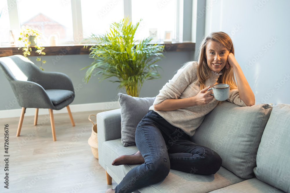 Woman enjoying a cup of coffee in winter at home. Shot of a young woman relaxing on her sofa with a cup of coffee. Young woman relaxing on the sofa at home with a warm beverage